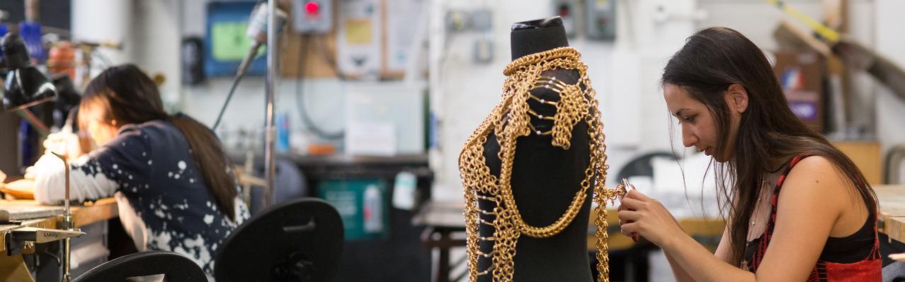 A student works with pliers on a chain-metal garment on a dress form